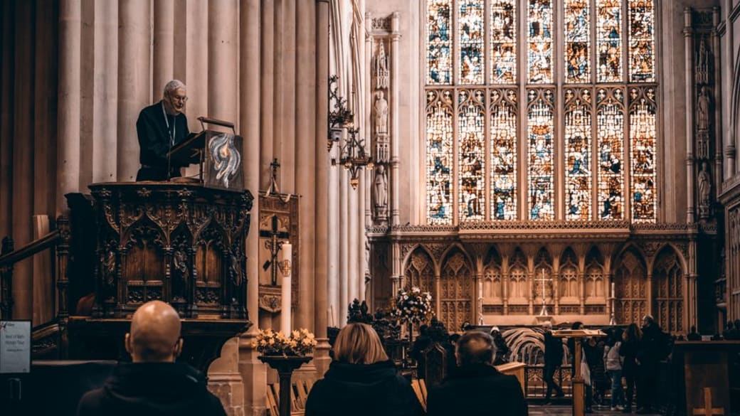 A sermon taking place inside Bath Abbey, showcasing Gothic architecture and stained glass windows.