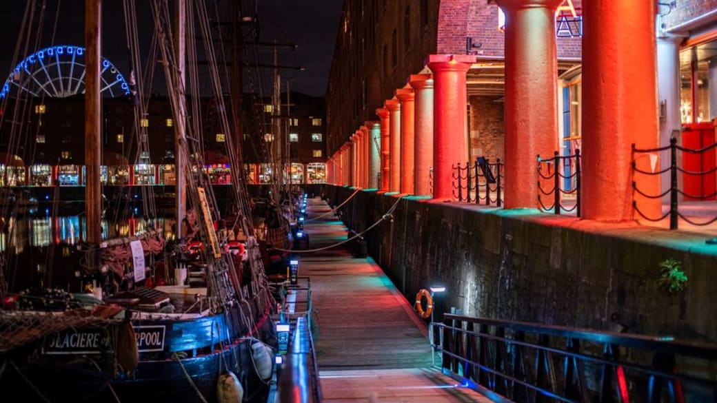 Atmospheric night scene of Liverpool's Royal Albert Dock with vibrant lights and boats.