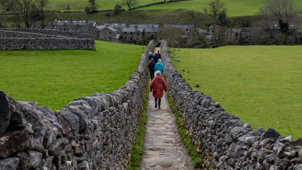 Group walking along stone path in Linton, Yorkshire Dales amidst scenic countryside views.