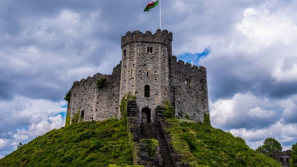 Majestic Cardiff Castle in Wales, topped by a flag, under dramatic cloudy skies.