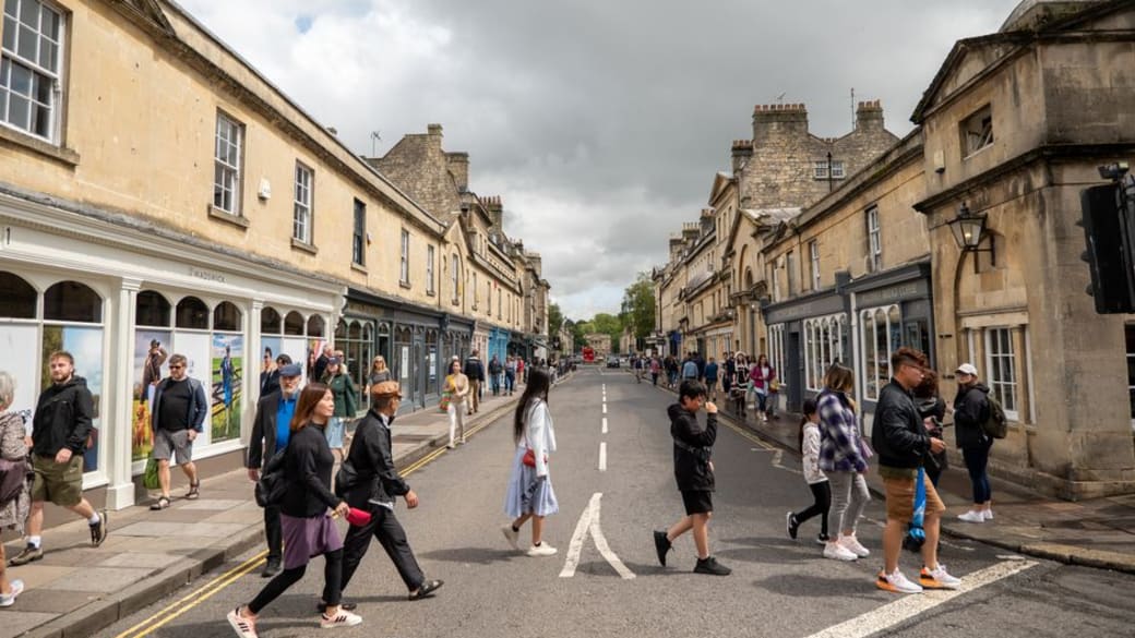 Crowds enjoying a bustling market square in Bath, UK, surrounded by elegant Georgian buildings and lively cafés.