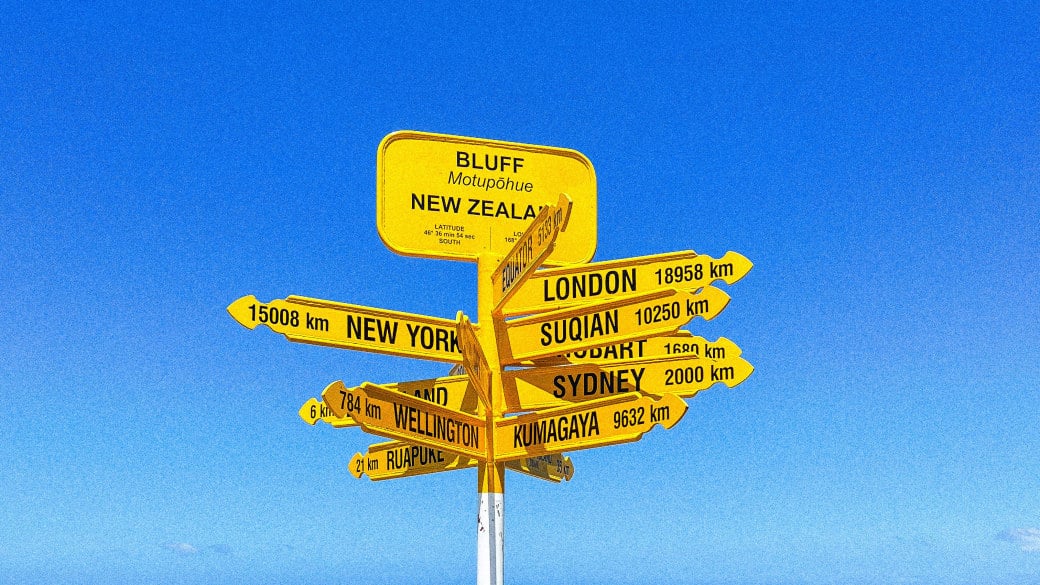 The vibrant Bluff sign at Stirling Point, indicating distances to famous cities around the world, against a backdrop of blight blue sky and sea.