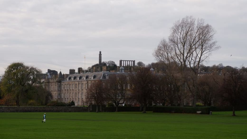 View of Holyrood Palace with lush lawn and cloudy sky in Edinburgh, Scotland.