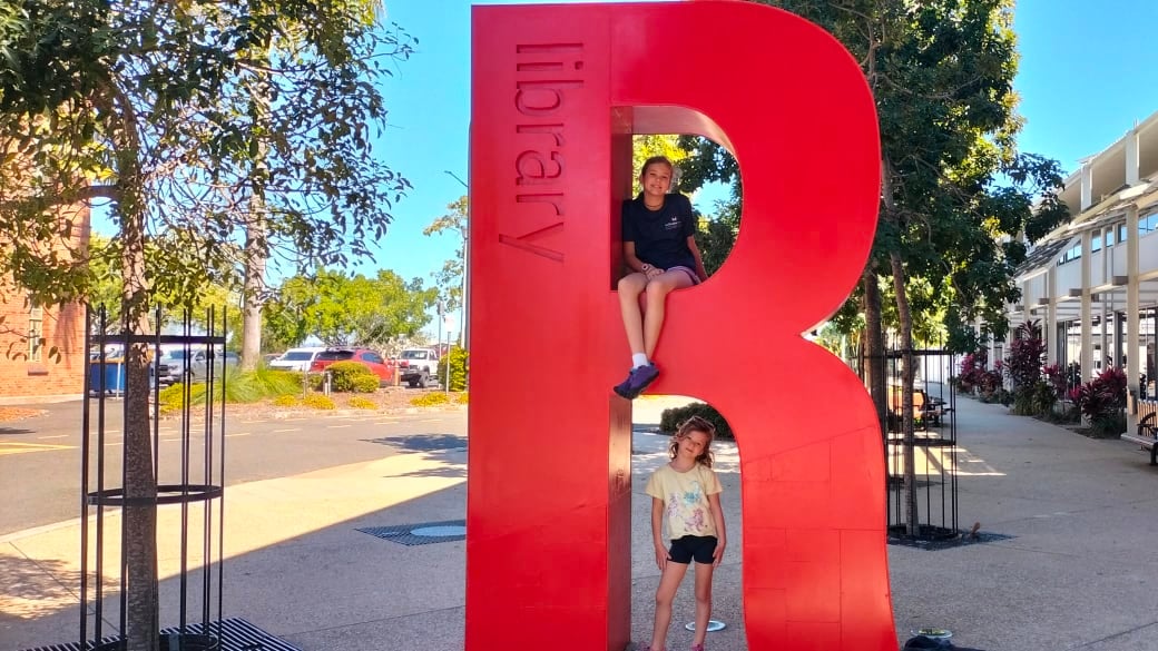 Ayla and Romy climb on a big, red, capital R out the front of the Rockhampton Library.