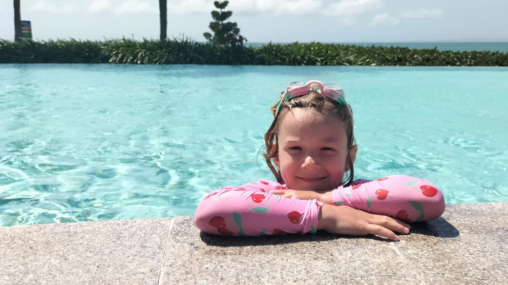 Romy rests on the edge of a large swimming pool at the Yeppoon Lagoon, with the ocean in the background.