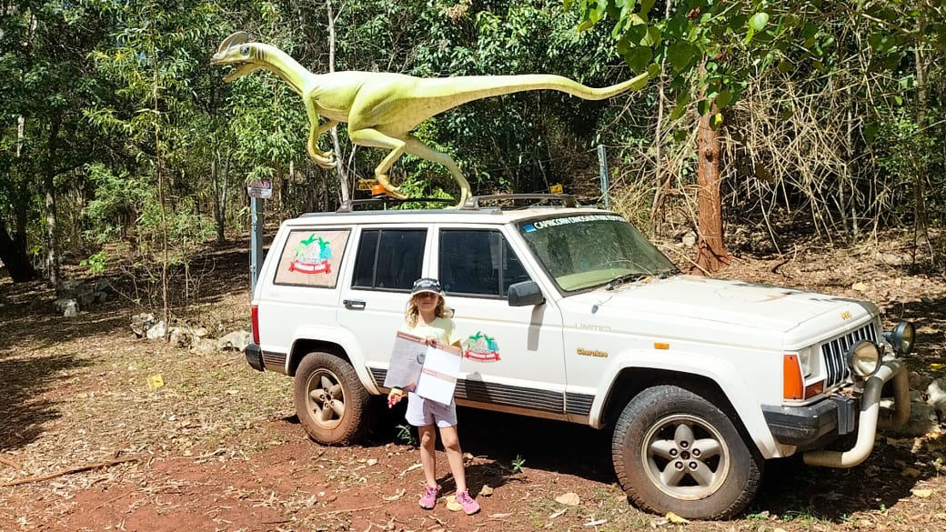 Romy stands in front of an offroad vehicle with a dinosaur on top and her park map in hand at the Yeppoon Dinosaur Park.